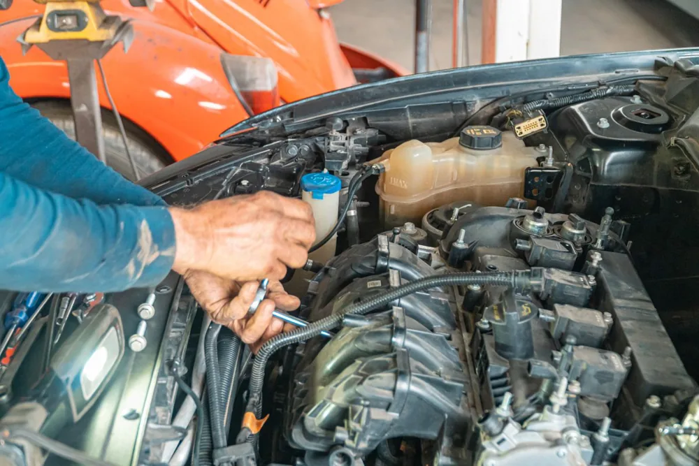 Mecânico trabalhando no motor de um carro; imagem ilustrativa